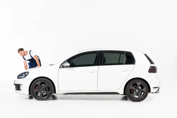 Handsome auto mechanic cleaning car after repairing on white — Stock Photo