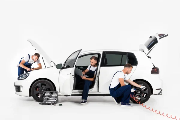 Schöner Automechaniker, der Reifen aufpumpt, Laptop benutzt und in Kapuze auf weiß schaut — Stockfoto