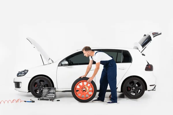 Vista laterale del meccanico auto spingendo pneumatico per cambiare quello vecchio su bianco — Foto stock