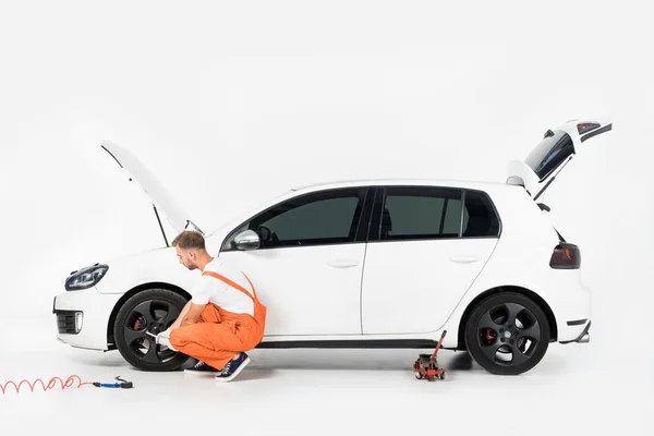 Automechaniker in orangefarbener Uniform wechselt Autoreifen auf weiß — Stockfoto