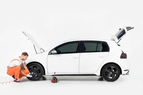 Side view of auto mechanic inflating tire and checking air with gauge pressure on white — Stock Photo