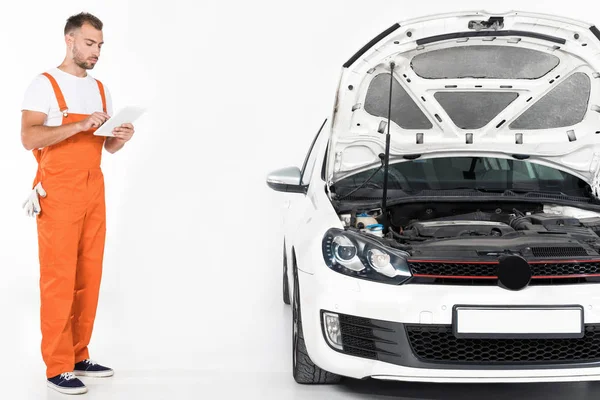 Schöner Automechaniker mit Tablet in der Nähe kaputtes Auto auf weiß — Stockfoto
