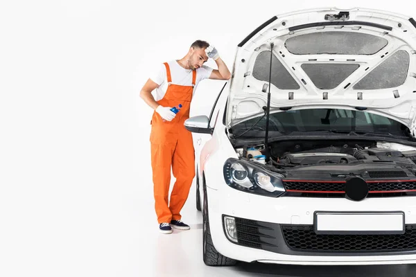 Tired auto mechanic holding bottle of water and leaning on car on white — Stock Photo