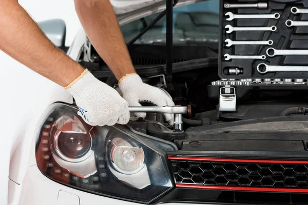 Abgeschnittenes Bild von Automechaniker Automechaniker Reparatur Auto mit Schraubenschlüssel auf weiß — Stockfoto