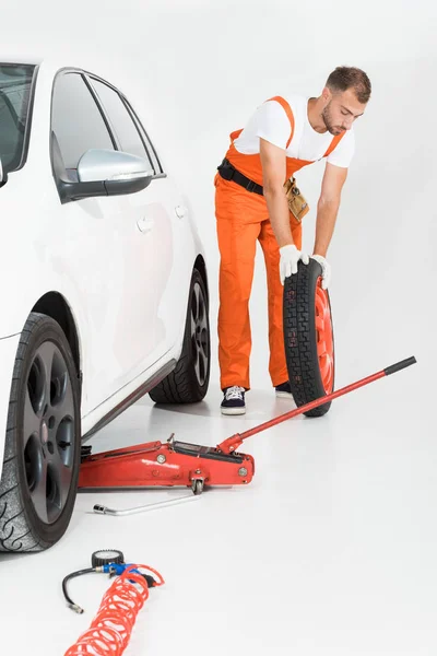 Auto mechanic rolling car tire on white — Stock Photo