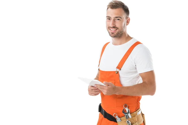 Portrait d'un beau et souriant mécanicien automobile en uniforme orange tenant comprimé isolé sur blanc — Photo de stock