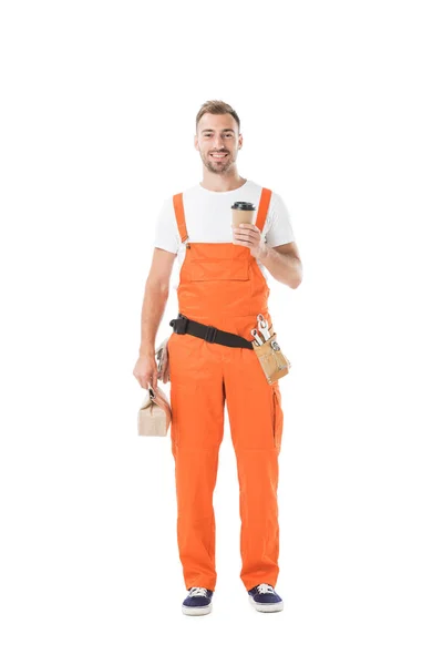 Sonriente mecánico auto guapo sosteniendo café para llevar y bolsa de papel con almuerzo aislado en blanco — Stock Photo