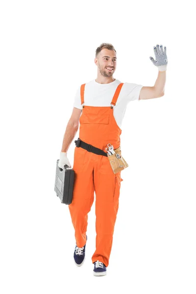 Schöner Automechaniker in orangefarbener Uniform mit Werkzeugkiste und winkender Hand isoliert auf weiß — Stockfoto
