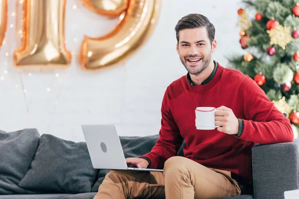 Homme heureux avec tasse de café à l'aide d'un ordinateur portable la veille de Noël — Photo de stock