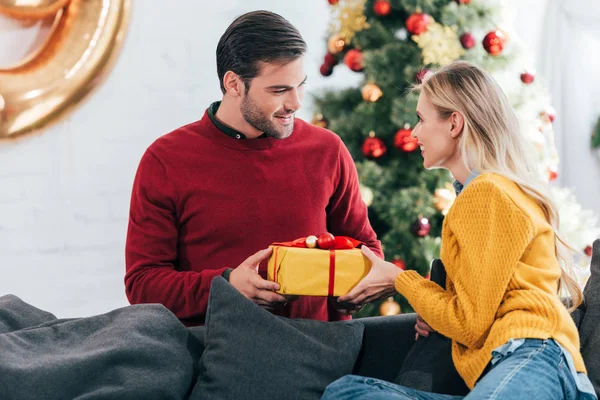 Presente de presente de casal feliz em casa com árvore de natal — Fotografia de Stock