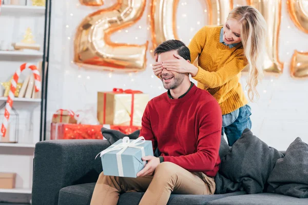 Menina fechar os olhos e fazer surpresa com o presente de ano novo para o namorado em casa com 2019 balões dourados — Fotografia de Stock