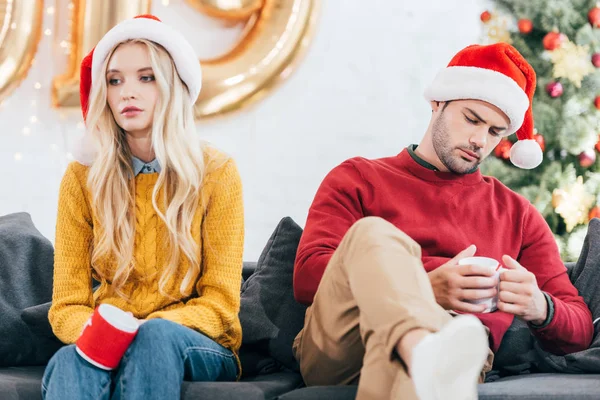 Chateado casal de mau humor segurando xícaras de café e sentado em casa na véspera de Natal — Fotografia de Stock
