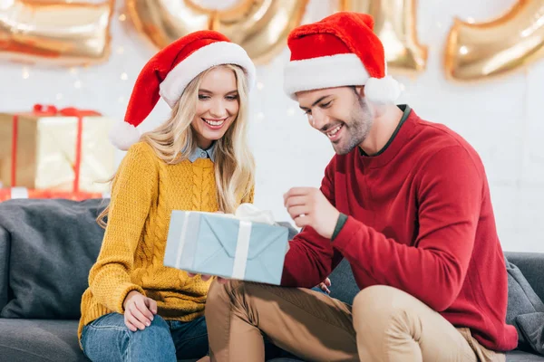Beautiful couple in santa hats with christmas gift at home — Stock Photo