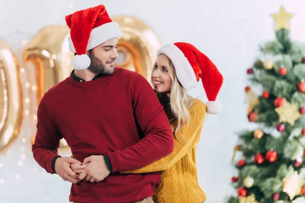 Happy girlfriend hugging her boyfriend at home with christmas tree — Stock Photo