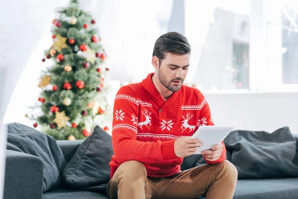Schöner Mann mit digitalem Tablet, Weihnachtsbaum dahinter — Stockfoto