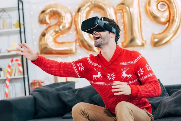 Возбужденный мужчина жестикулирует и использует гарнитуру виртуальной реальности в 2019 году — стоковое фото