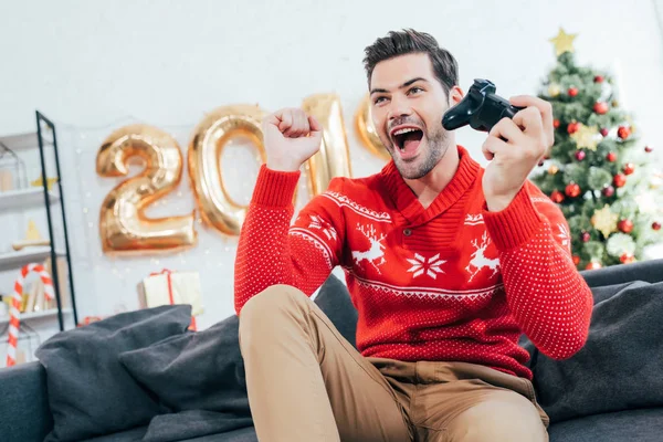 Hombre emocionado jugando videojuego con joystick durante la Navidad - foto de stock