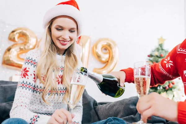 Чоловік наливає шампанське в окуляри для жінки вдома з новорічними кульками 2019 року — стокове фото