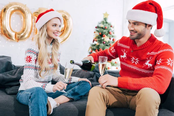Uomo sorridente versando champagne in bicchieri e coppia che celebra il Natale a casa — Foto stock