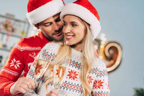 Lächelndes Paar in Weihnachtsmützen, das an Heiligabend mit Sektgläsern klingelt — Stockfoto