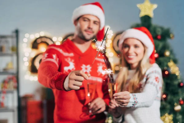 Foco seletivo do casal em chapéus santa segurando sparklers no Natal — Fotografia de Stock
