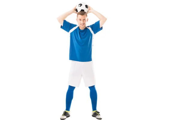 Ganzkörperansicht des glücklichen jungen Fußballers, der den Ball über dem Kopf hält und isoliert auf weiß in die Kamera lächelt — Stockfoto
