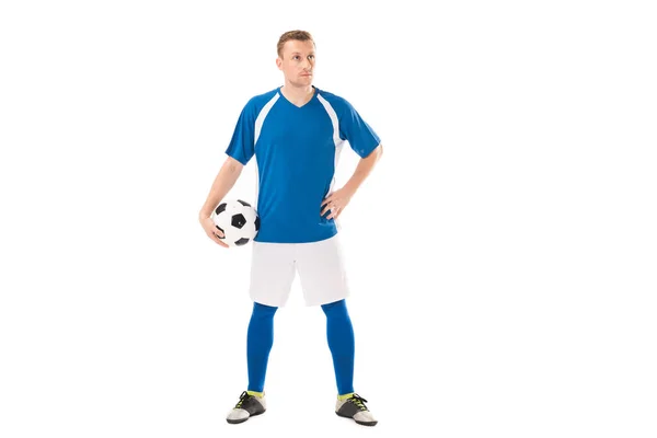 Confiado joven jugador de fútbol sosteniendo la pelota y mirando hacia otro lado aislado en blanco - foto de stock