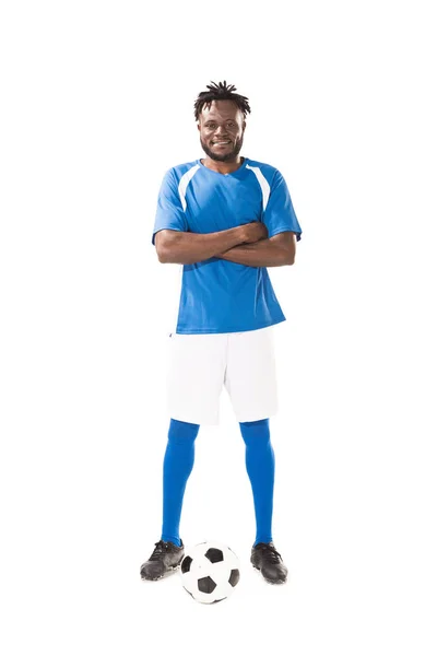 Полный вид улыбающегося африканского футболиста, стоящего со скрещенными руками и смотрящего на камеру, изолированную на белом — стоковое фото