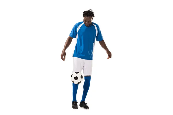 Hombre afroamericano deportivo en uniforme de fútbol jugando con pelota aislada en blanco - foto de stock