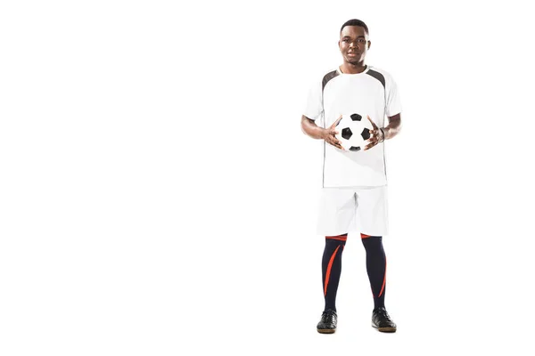 Vista completa de feliz joven afroamericano jugador de fútbol sosteniendo la pelota y sonriendo a la cámara aislado en blanco - foto de stock