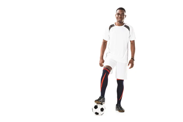 Guapo joven afroamericano deportista de pie con pelota de fútbol y sonriendo a la cámara aislado en blanco - foto de stock