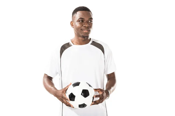 Lächelnder junger afrikanisch-amerikanischer Sportler, der einen Fußballball in der Hand hält und isoliert auf weißem Grund wegschaut — Stockfoto