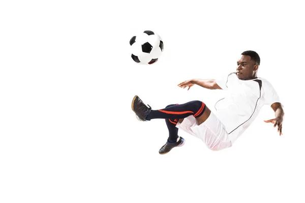 Athletic young african american soccer player kicking ball in jump isolated on white — Stock Photo