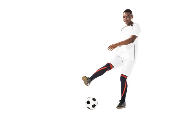 Jovem jogador de futebol afro-americano chutando bola e sorrindo para a câmera isolada no branco — Fotografia de Stock