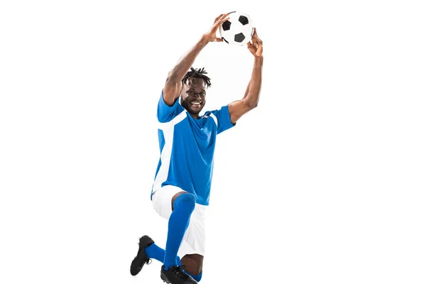 Felice giocatore di calcio afroamericano tenendo la palla sopra la testa e sorridendo alla fotocamera isolata sul bianco — Foto stock