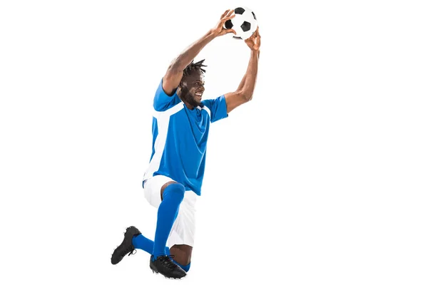 Feliz afroamericano deportista arrodillado y sosteniendo pelota de fútbol aislado en blanco - foto de stock