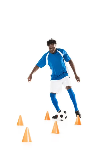 Jovem esportista afro-americano treinando com bola de futebol e cones marcadores isolados em branco — Fotografia de Stock