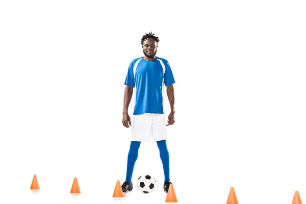 Sorrindo jovem jogador de futebol afro-americano treinando com cones de bola e marcador isolados em branco — Fotografia de Stock