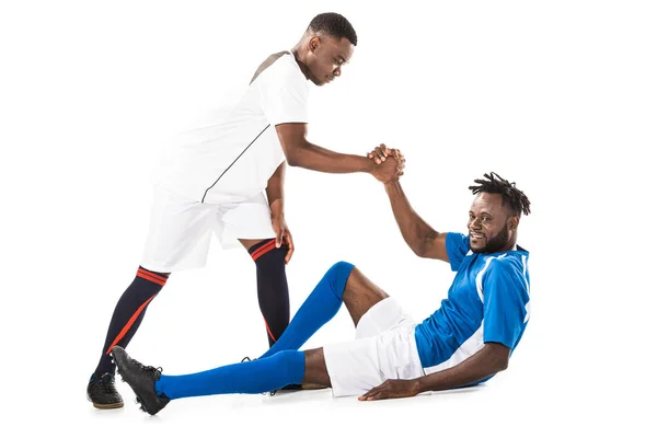 Jovem esportista afro-americano ajudando jogador de futebol deitado isolado no branco — Fotografia de Stock