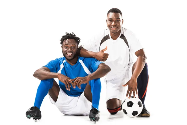 Feliz afroamericano futbolistas sonriendo a la cámara y mostrando el pulgar hacia arriba aislado en blanco - foto de stock