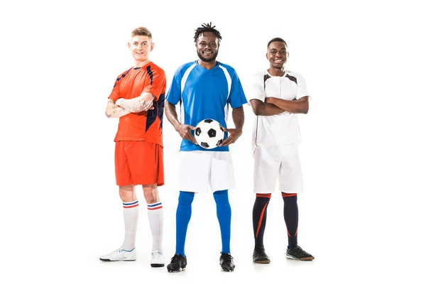 Vista completa de jugadores multiétnicos jóvenes de fútbol de pie juntos y sonriendo a la cámara aislada en blanco - foto de stock