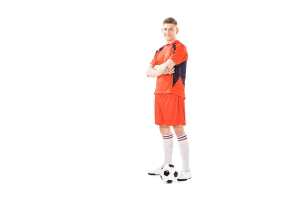 Полный вид спортивного молодого футболиста, стоящего со скрещенными руками и улыбающегося в камеру, изолированную на белом — стоковое фото