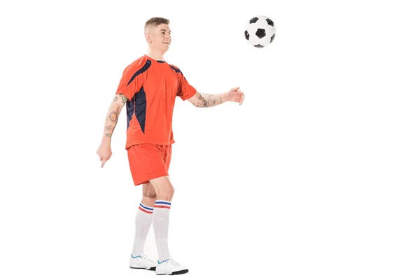 Vista completa de sonriente joven futbolista pateando pelota aislado en blanco - foto de stock