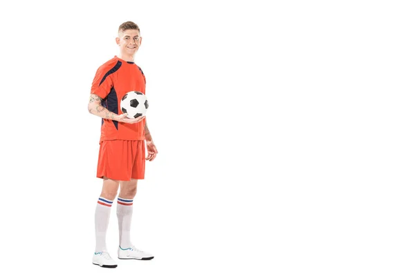 Piena vista lunghezza del bel giovane giocatore di calcio tenendo palla e sorridendo alla fotocamera isolata su bianco — Foto stock