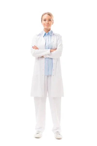 Привлекательная молодая врач со скрещенными руками, смотрящая на камеру, изолированную на белом — стоковое фото