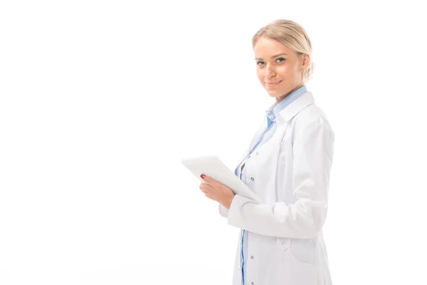 Glückliche junge Ärztin, die mit Tablette arbeitet und isoliert auf weiße Kamera schaut — Stockfoto