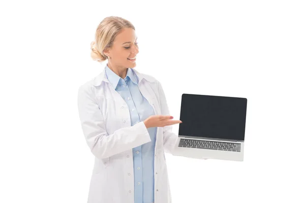 Sourire jeune médecin femme pointant vers un ordinateur portable avec écran blanc isolé sur blanc — Photo de stock