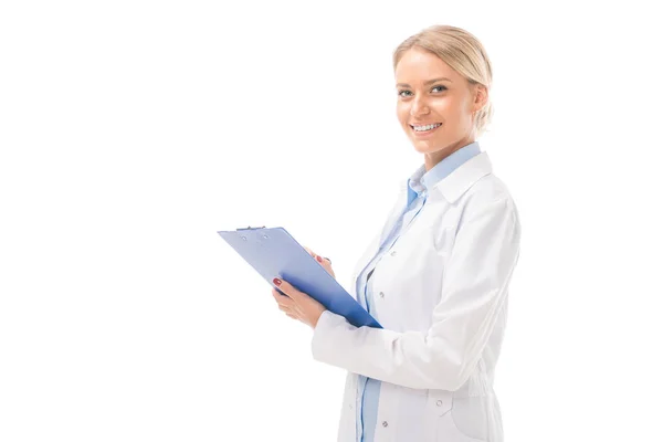 Feliz joven médico escribiendo en portapapeles mirando a la cámara aislada en blanco - foto de stock