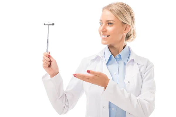Smiling young female neurologist pointing at reflex hammer isolated on white — Stock Photo