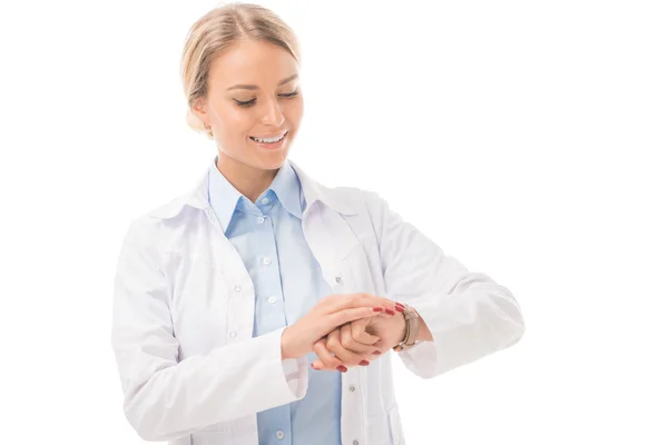 Lächelnde junge Ärztin bei der Zeitkontrolle mit Armbanduhr isoliert auf weiß — Stockfoto